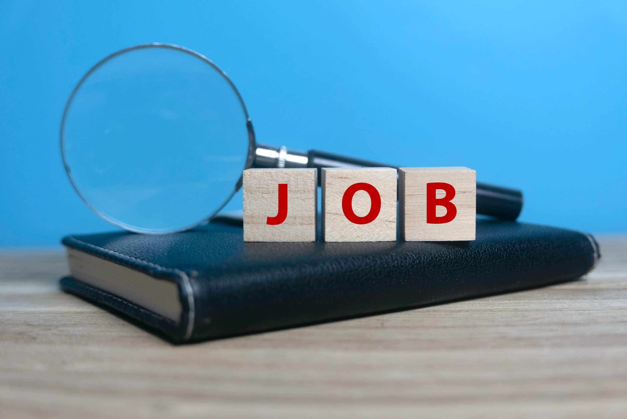 Wooden blocks spelling “JOB” beside a magnifying glass remind people to start job hunting.